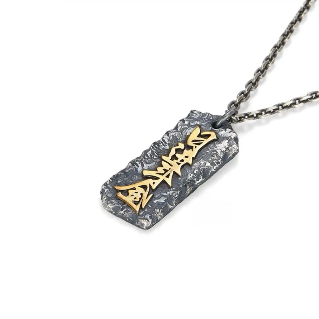 Angled shot of the Abundance necklace, highlighting the rugged silver texture and raised gold calligraphy