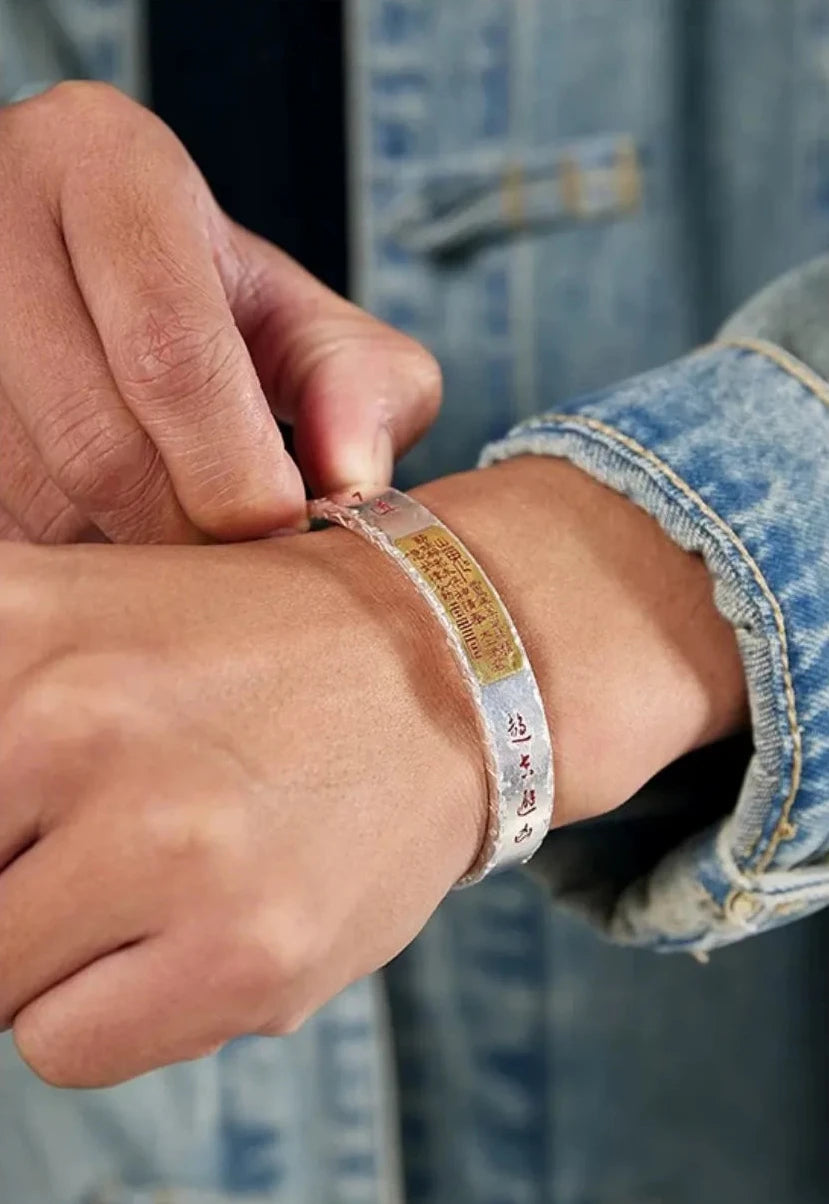 Close-up of hands adjusting the fit of the silver cuff, showing the gold talisman detail against the skin