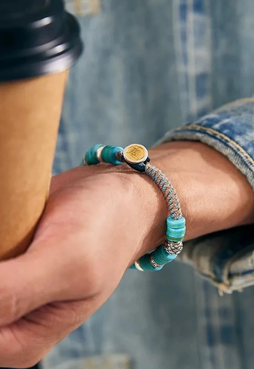 Lifestyle shot of a man holding a coffee cup, focusing on the gold coin toggle clasp and the rugged braided detail against a denim jacket