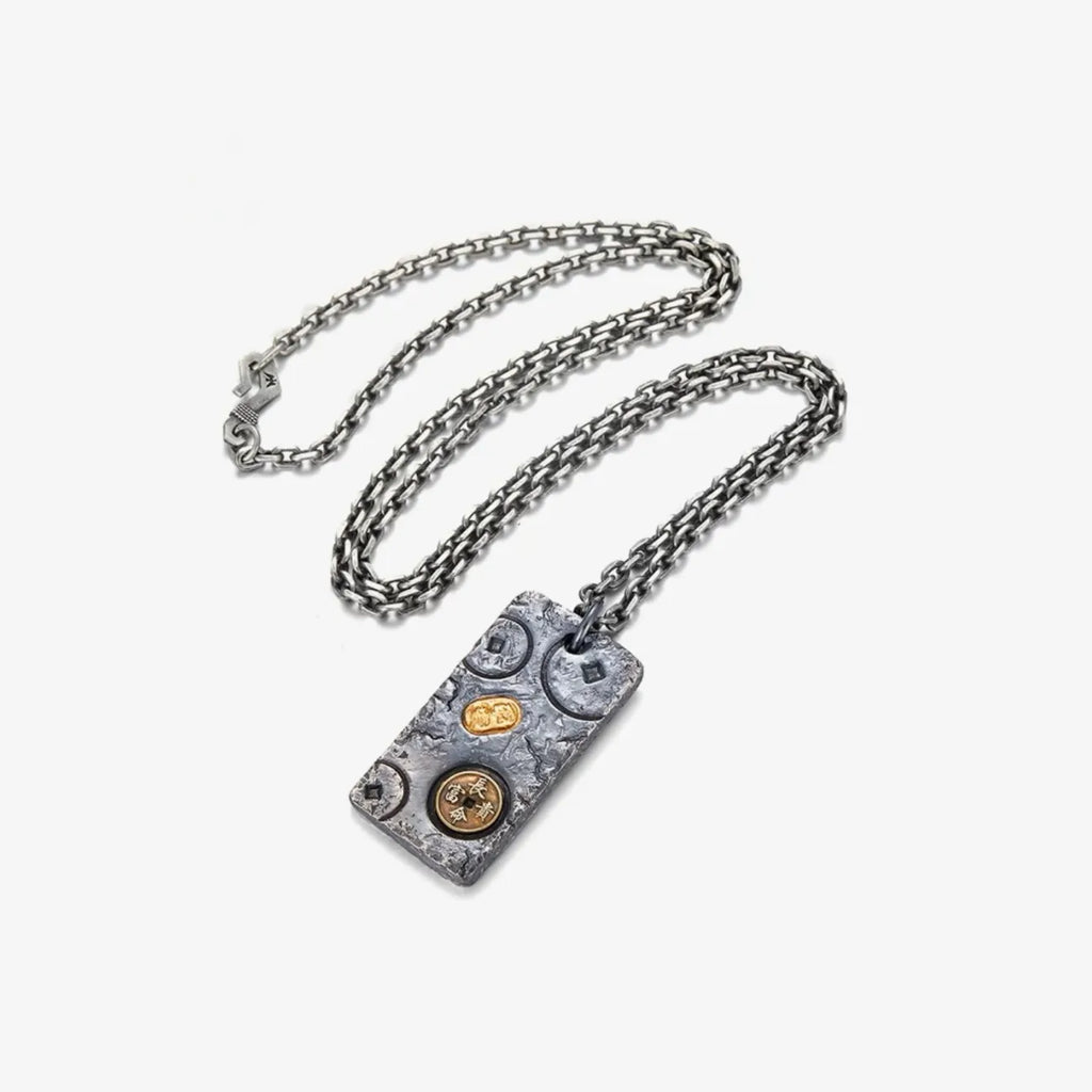 Flat lay of the fortune necklace featuring ancient coins and a gold ingot relief on a hammered silver texture