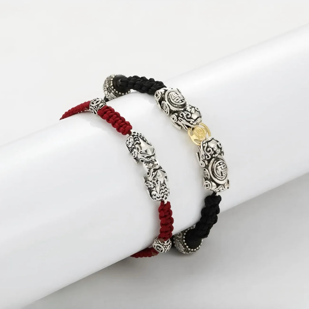 Front view of the matching Feng Shui bracelet set: a black rope bracelet with a large coin-eating Pixiu and a red rope bracelet with a delicate silver Pixiu