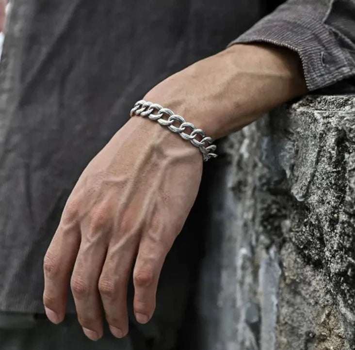 Lifestyle shot of a man in a grey corduroy shirt wearing the textured silver quill bracelet against a stone wall