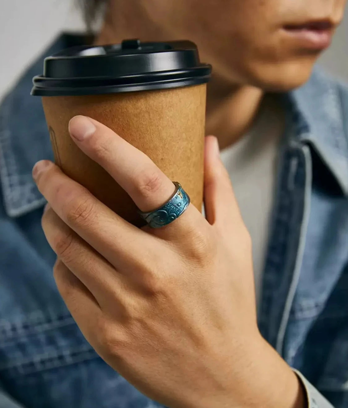 Model holding a coffee cup wearing the blue patina Aspiration Ring, displaying the vibrant bluing color and gold star details
