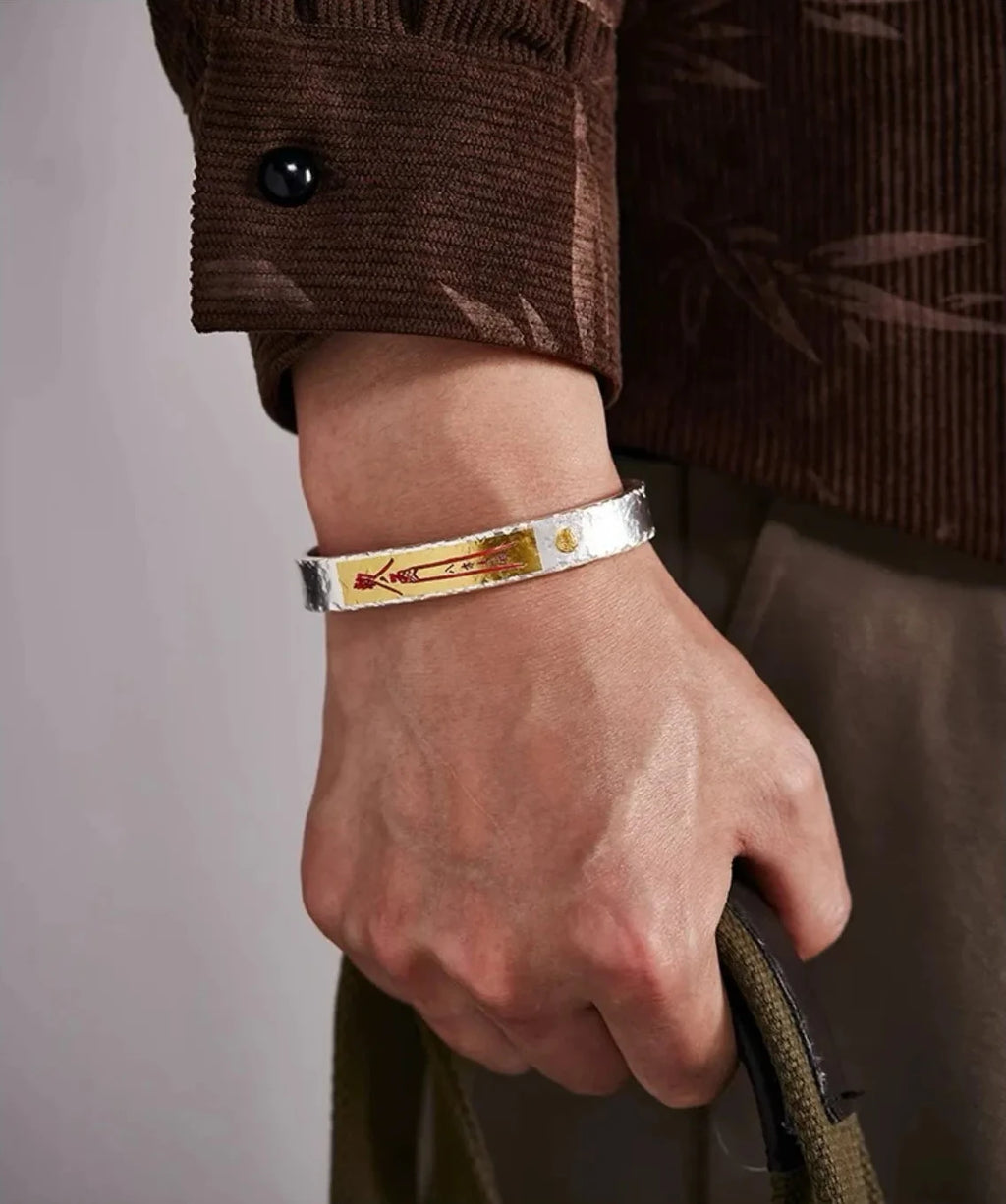 Lifestyle shot of a man holding a bag, wearing the Money Bangle which complements the brown corduroy shirt with its rustic aesthetic