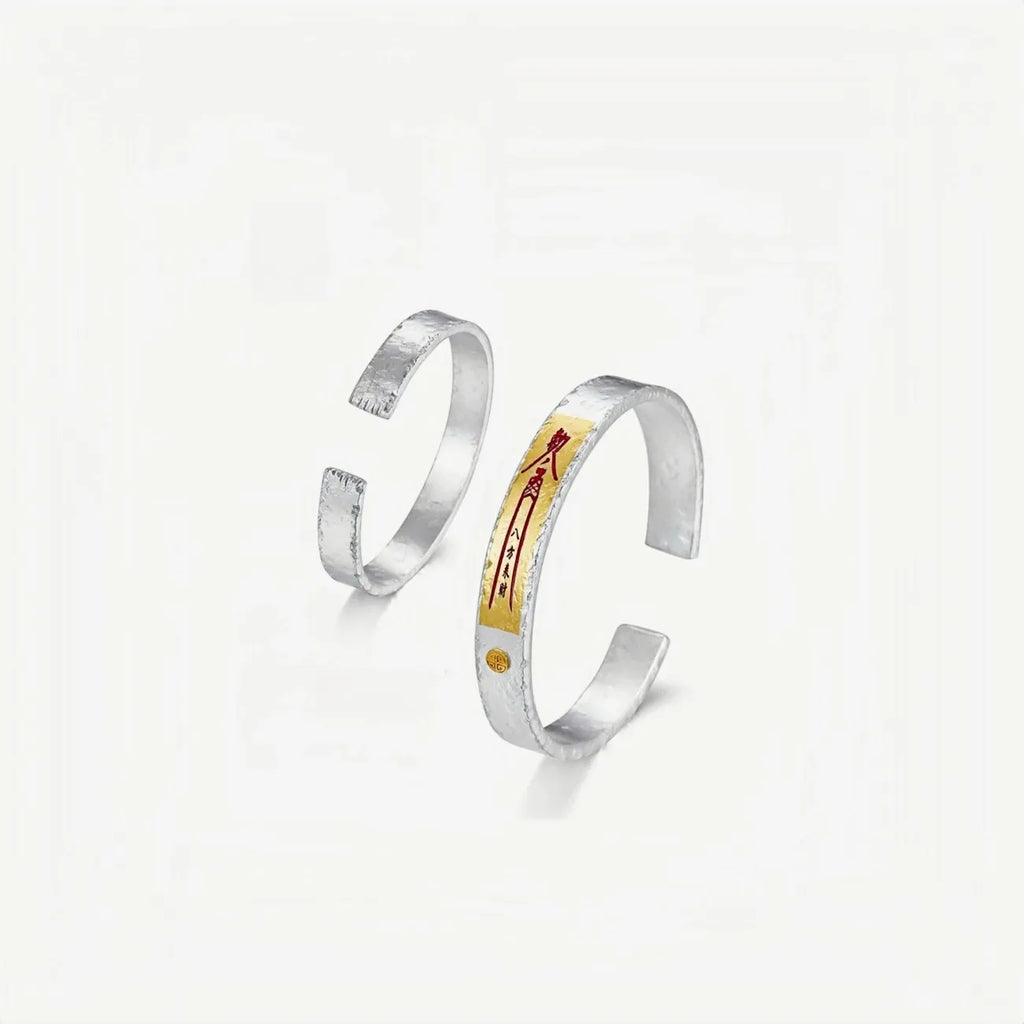 A pair of silver and gold bangles displayed together, showcasing the open cuff design and the consistency of the artisan craftsmanship