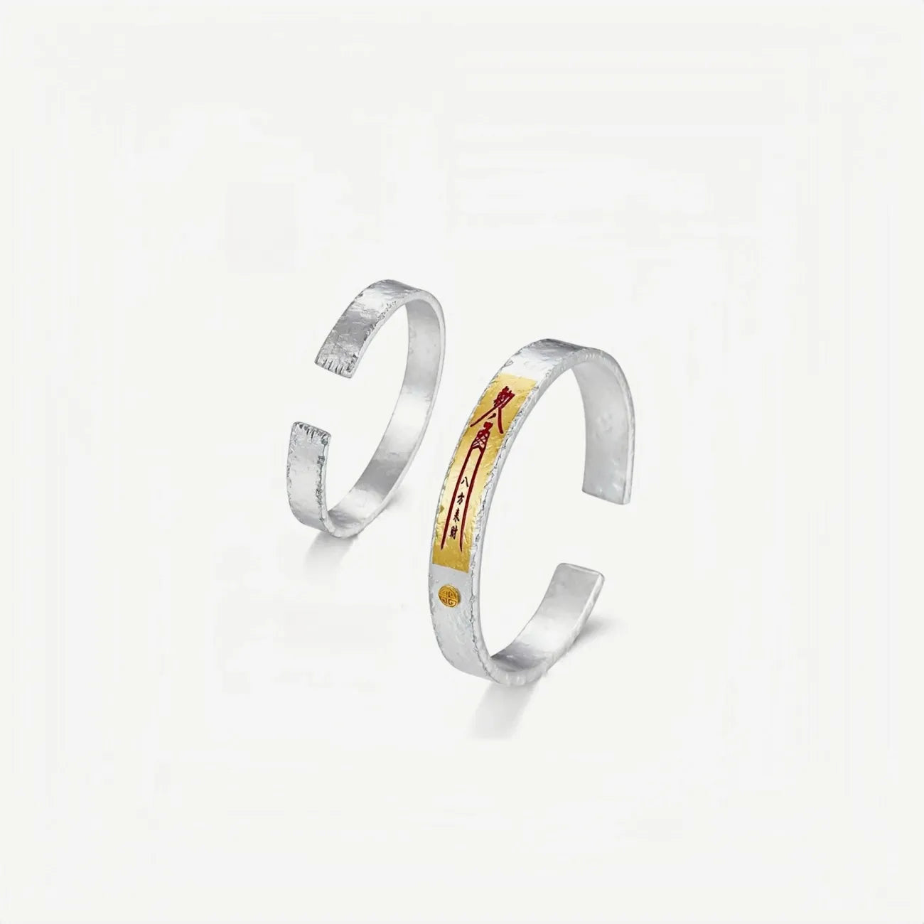 A pair of silver and gold bangles displayed together, showcasing the open cuff design and the consistency of the artisan craftsmanship