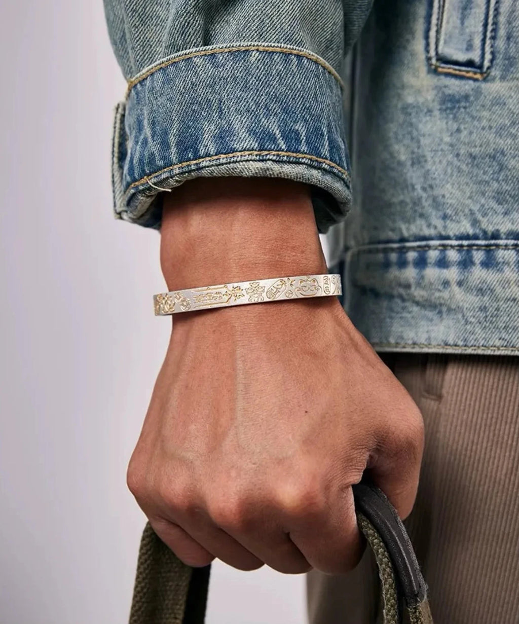 Lifestyle shot of a man wearing a denim jacket holding a bag, with the Fortune Bangle adding a touch of cultural flair to the outfit