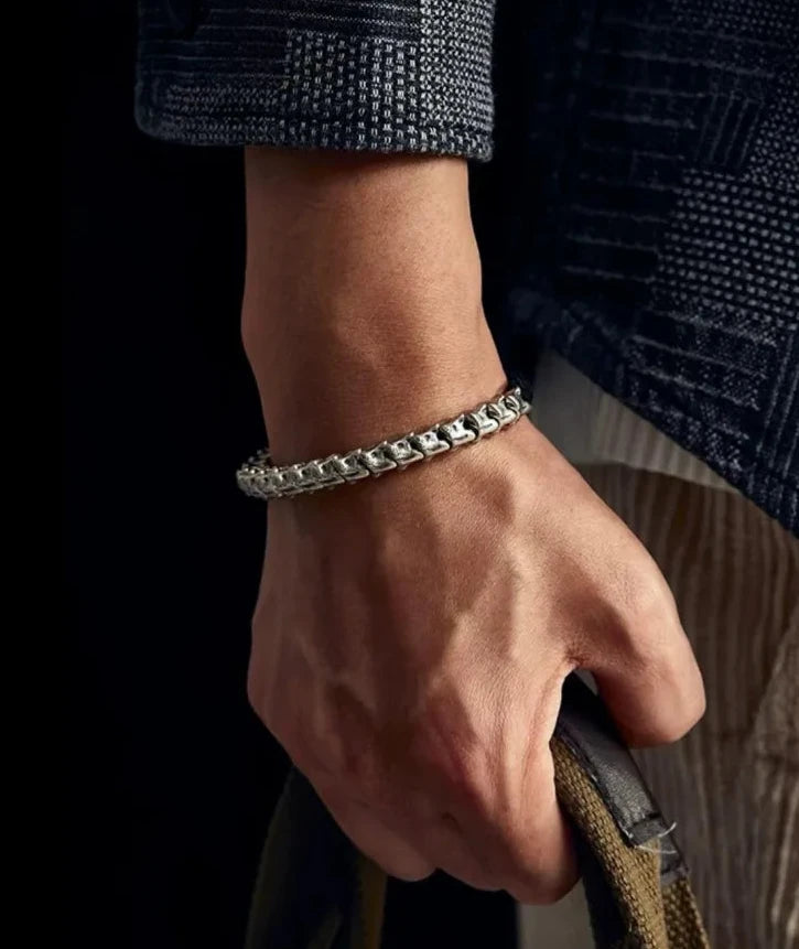 Lifestyle shot of a man holding a bag, wearing the silver bone bracelet with a casual checkered shirt