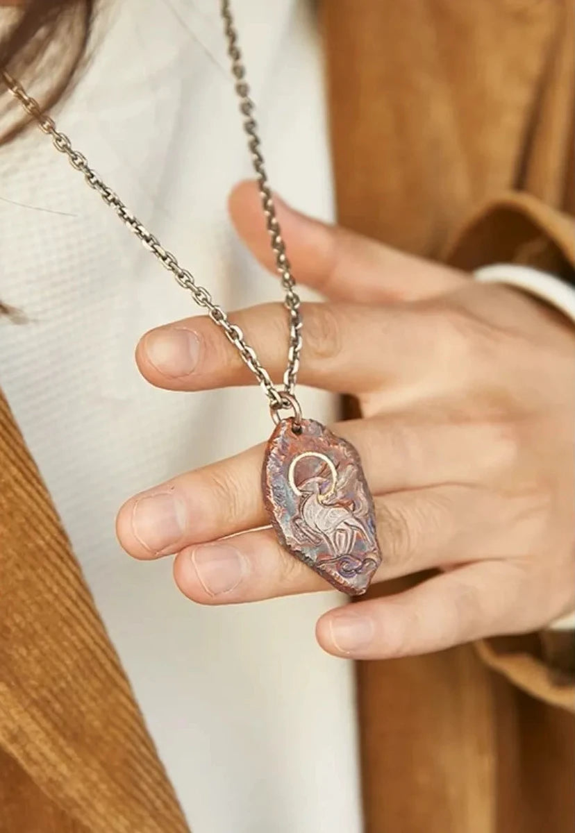 Close-up of a hand holding the rufous bronze Celestial Stag pendant, highlighting the details