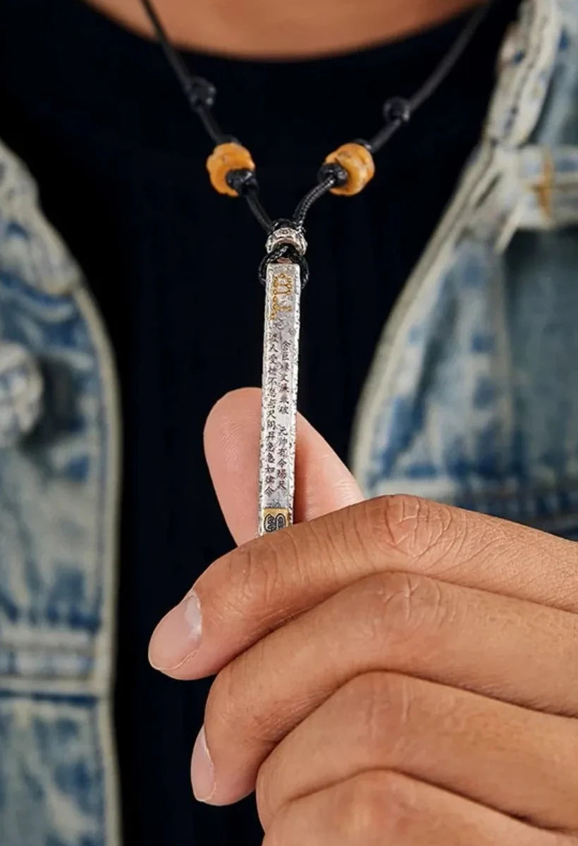 Close-up of a hand holding the silver talisman pendant, revealing the 'urgent order' mantra and bottom seal