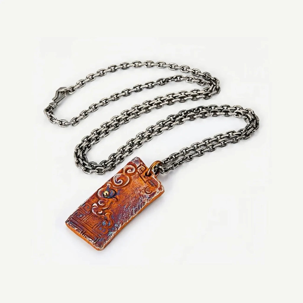 Flat lay of the auspicious cloud necklace featuring a rectangular pendant with rufous and bluing patina and a silver chain