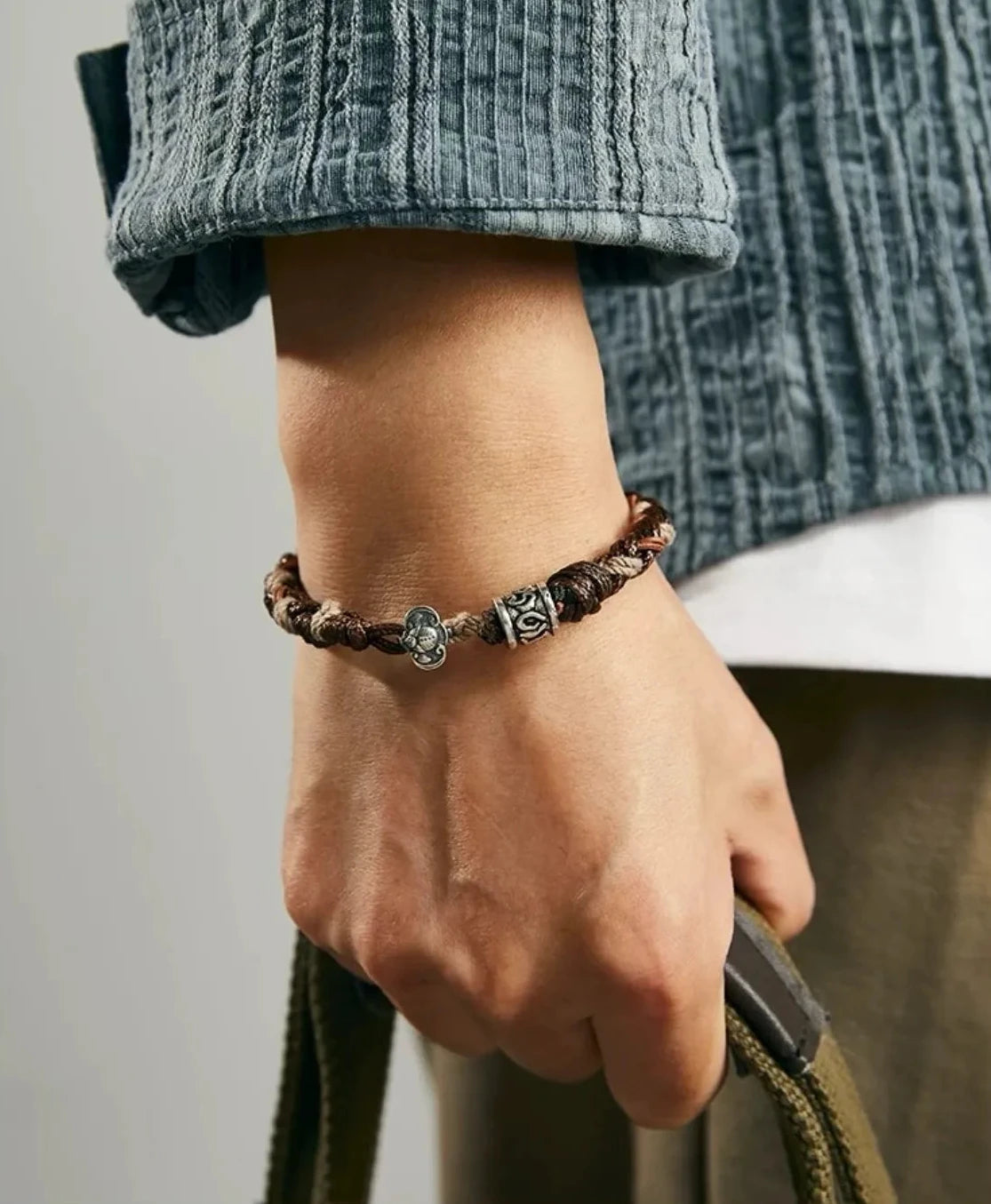 Lifestyle shot of a man holding a bag, wearing the earth-tone braided bracelet which complements a casual, rugged look