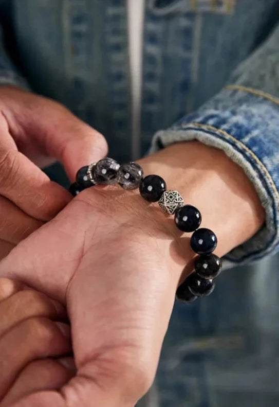 Close-up detail of the bracelet on a male wrist, showing the reflective sheen of the blue stones and the raw crystal focal point