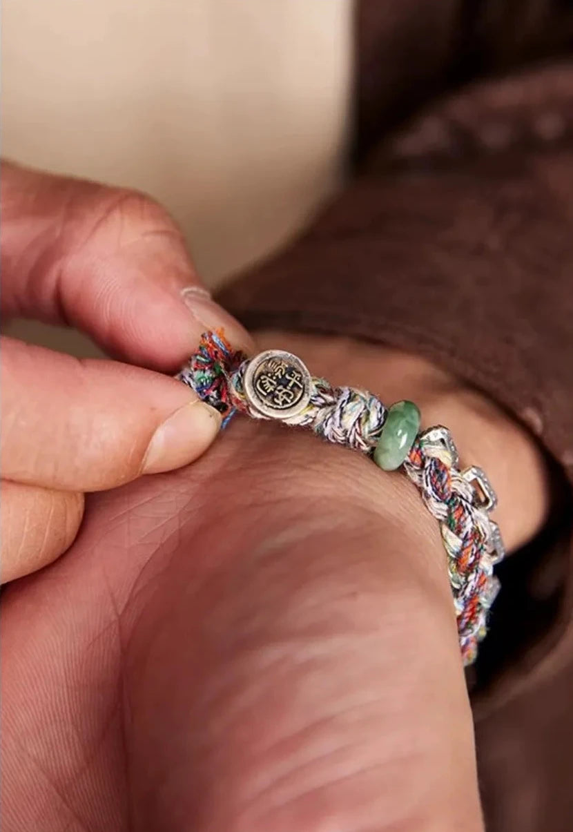 Close-up detail of the adjustable closure, featuring a natural green jadeite bead acting as a slider for the lucky coin charm