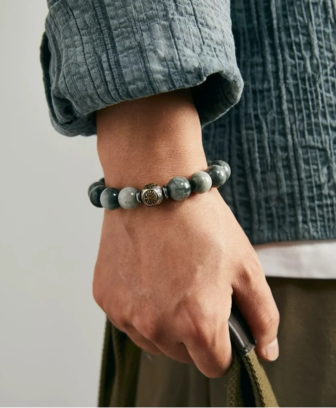 Lifestyle shot of a man holding a bag, wearing the grey eagle eye bracelet that complements a textured grey shirt