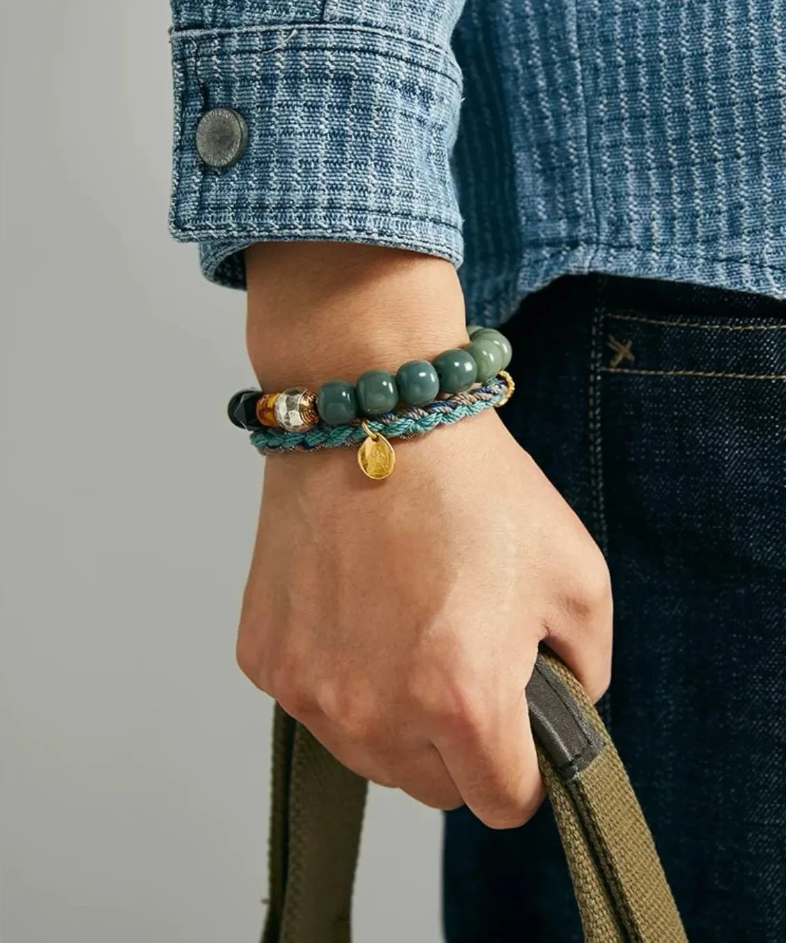 Close-up on the wrist focusing on the gold Prajna/Buddha charm and the rich texture of the green opal beads
