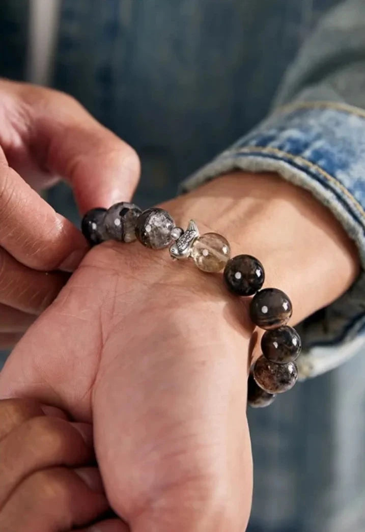 Lifestyle shot focusing on the silver bird charm and the single golden rutilated quartz bead, symbolizing good luck