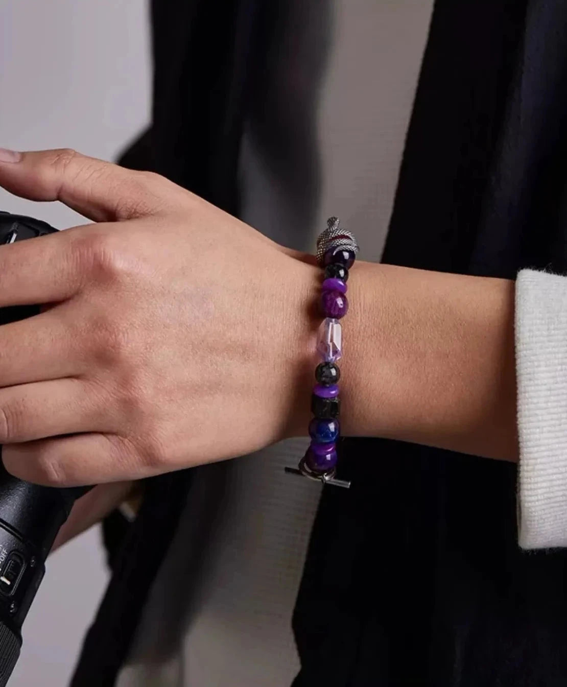 A photographer holding a camera, showcasing the purple gemstone side of the bracelet, symbolizing creativity and insight