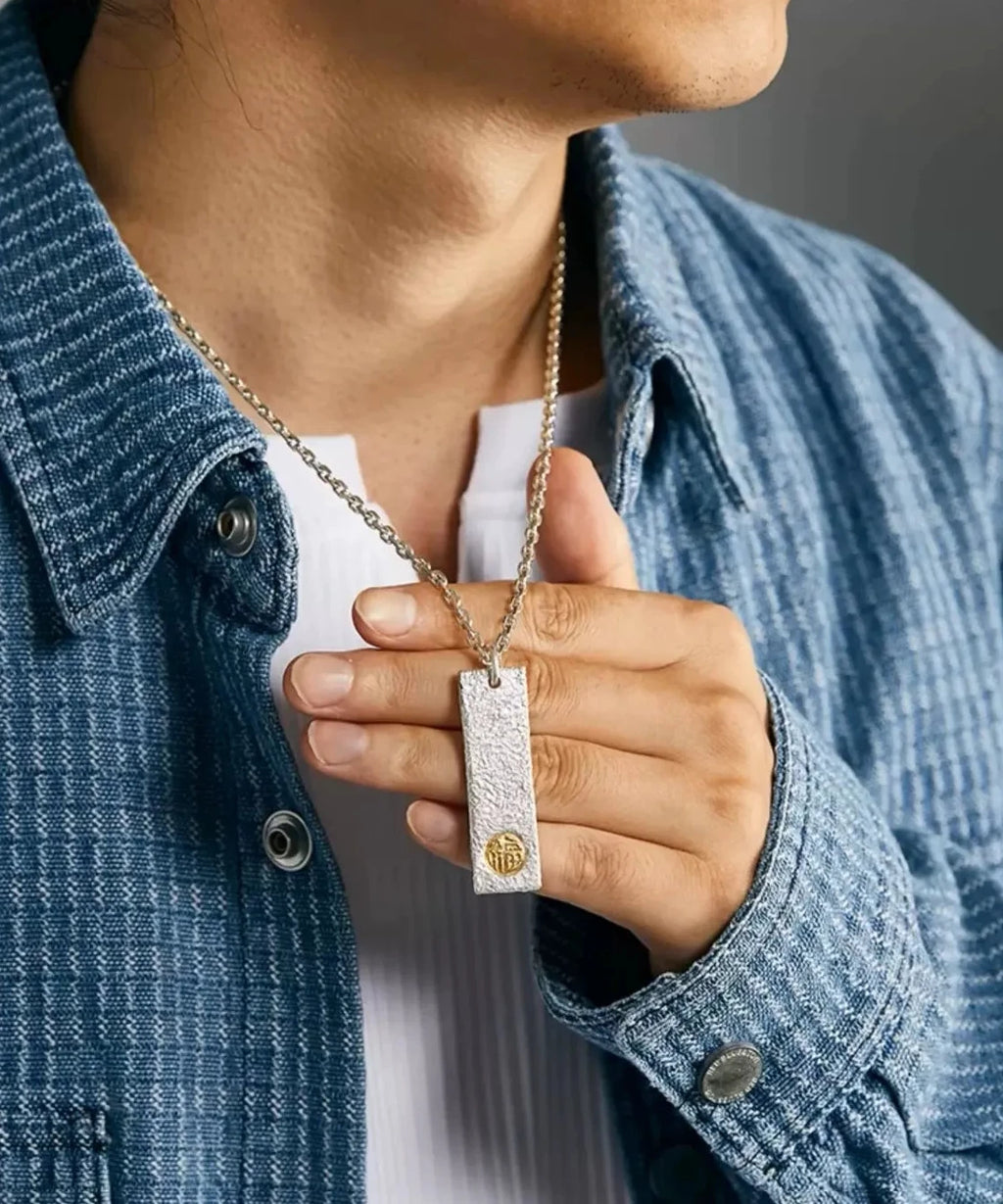 Close-up of a model holding the silver bar pendant against a white shirt, showing size and detail