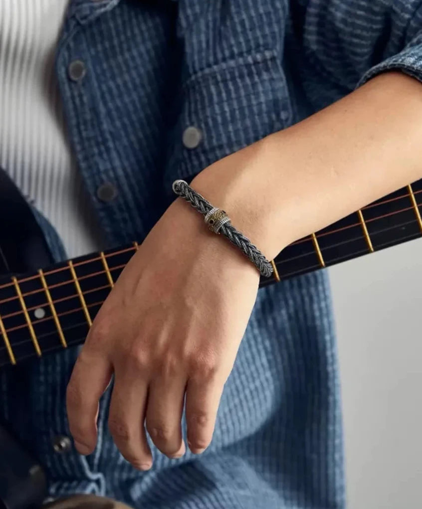 A close-up of a guitarist's hand resting on an acoustic guitar, showcasing the bracelet as a symbol of creativity