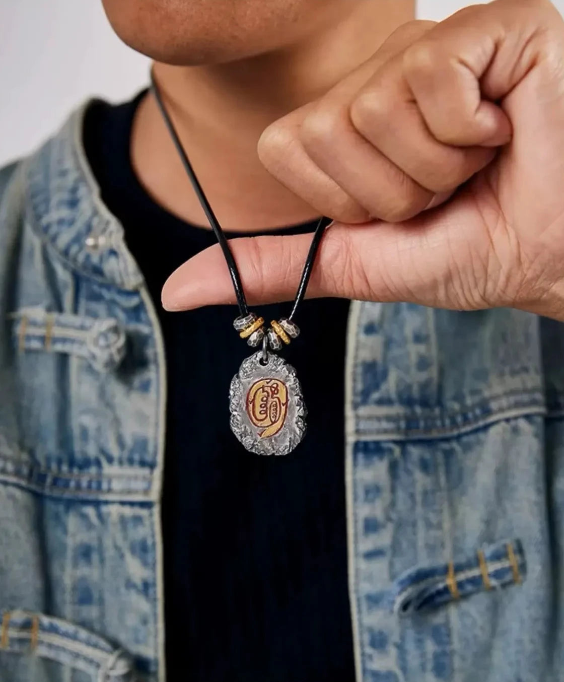 Model in a denim jacket holding the Incantation necklace, showcasing the pendant's size and design