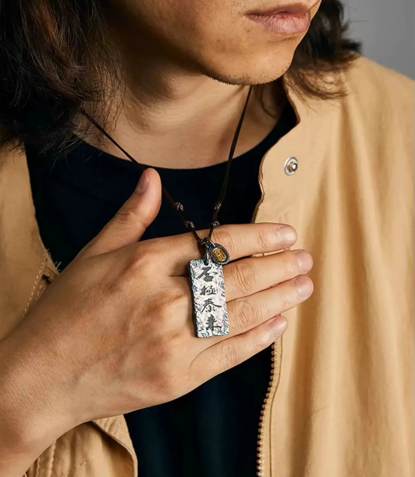 Close-up of a hand holding the Fortune's Turn necklace, showing the detailed silver texture and golden bronze elements