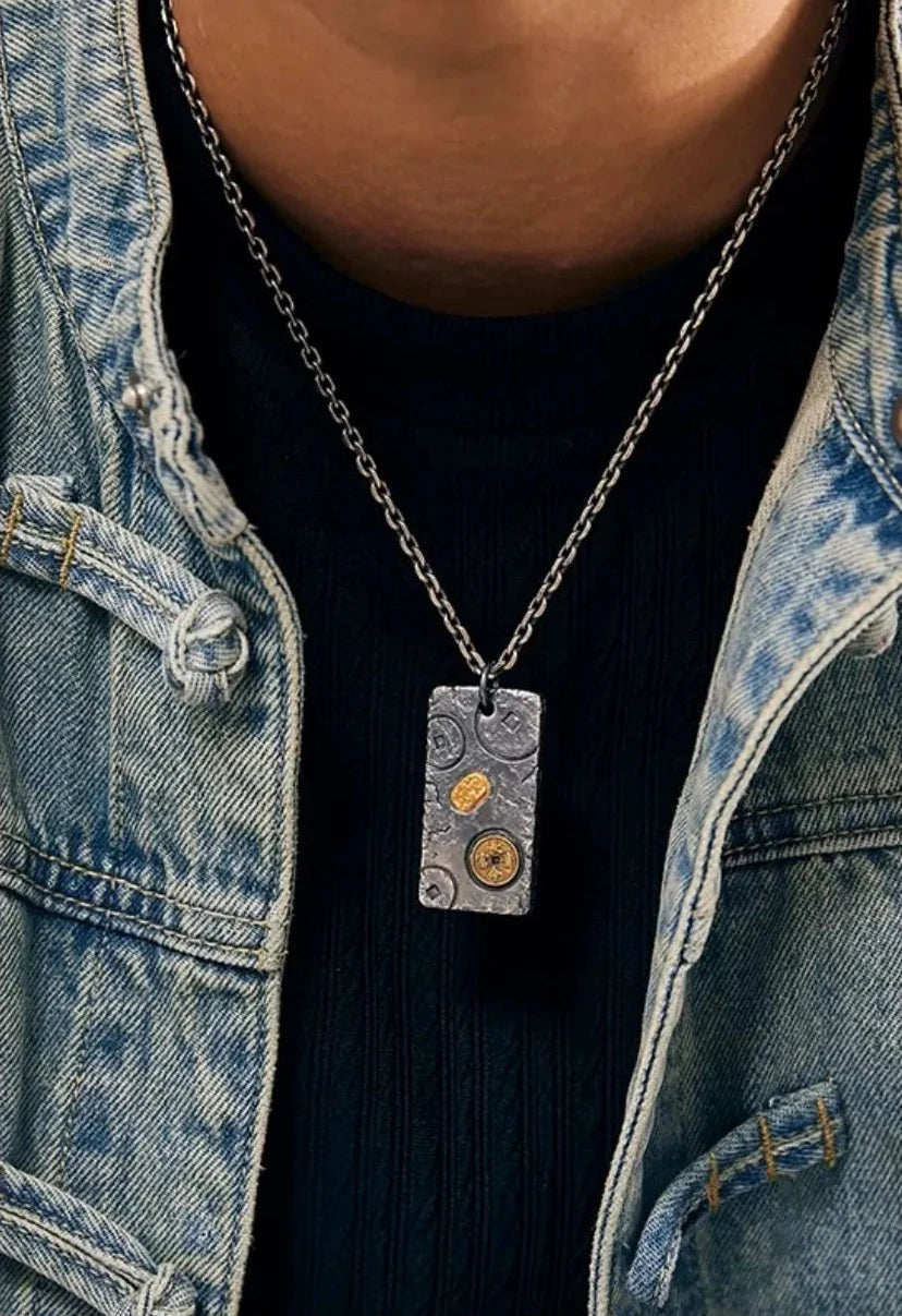 Close-up chest view of the silver and gold fortune pendant worn over a black ribbed shirt