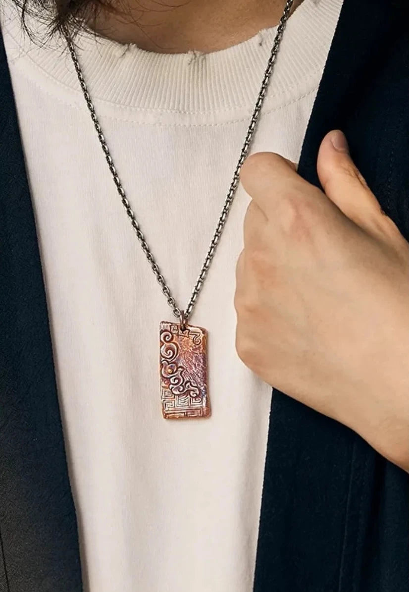 Man wearing the serenity necklace styled with a black cardigan and white shirt, hand pulling the collar