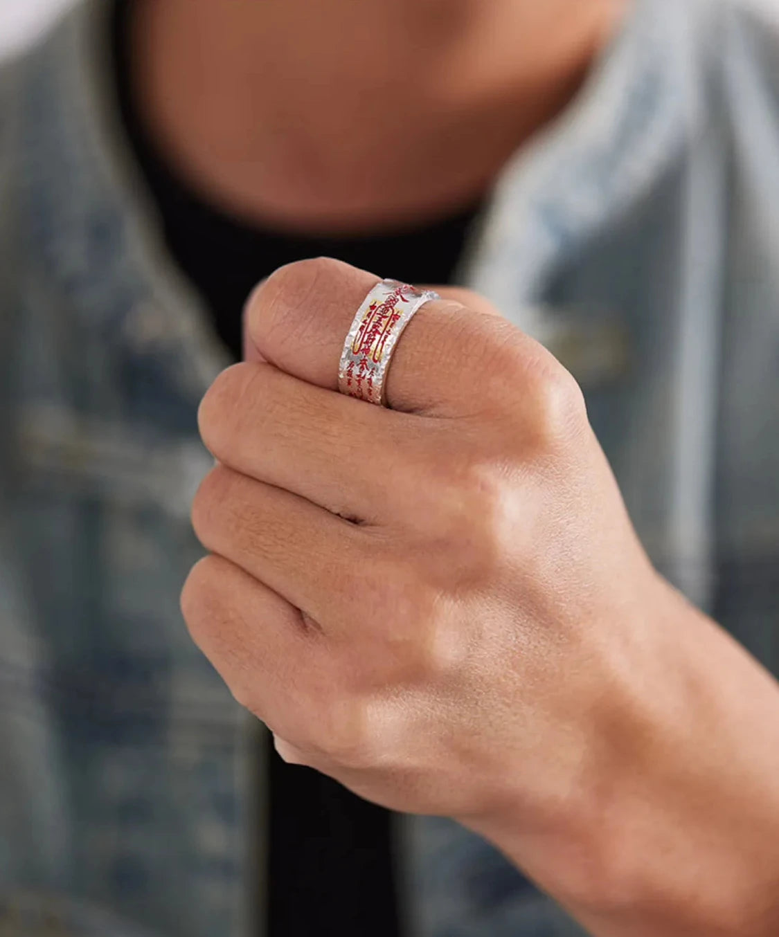 Lifestyle shot of a man wearing the crinkled silver amulet ring with a denim jacket, holding a bag strap