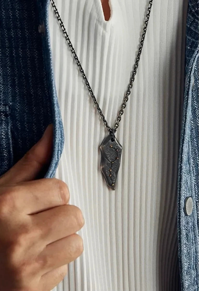 Man wearing a rustic oxidized silver arrowhead pendant with gold star constellation inlay, styled with a sashiko denim shirt and carabiner