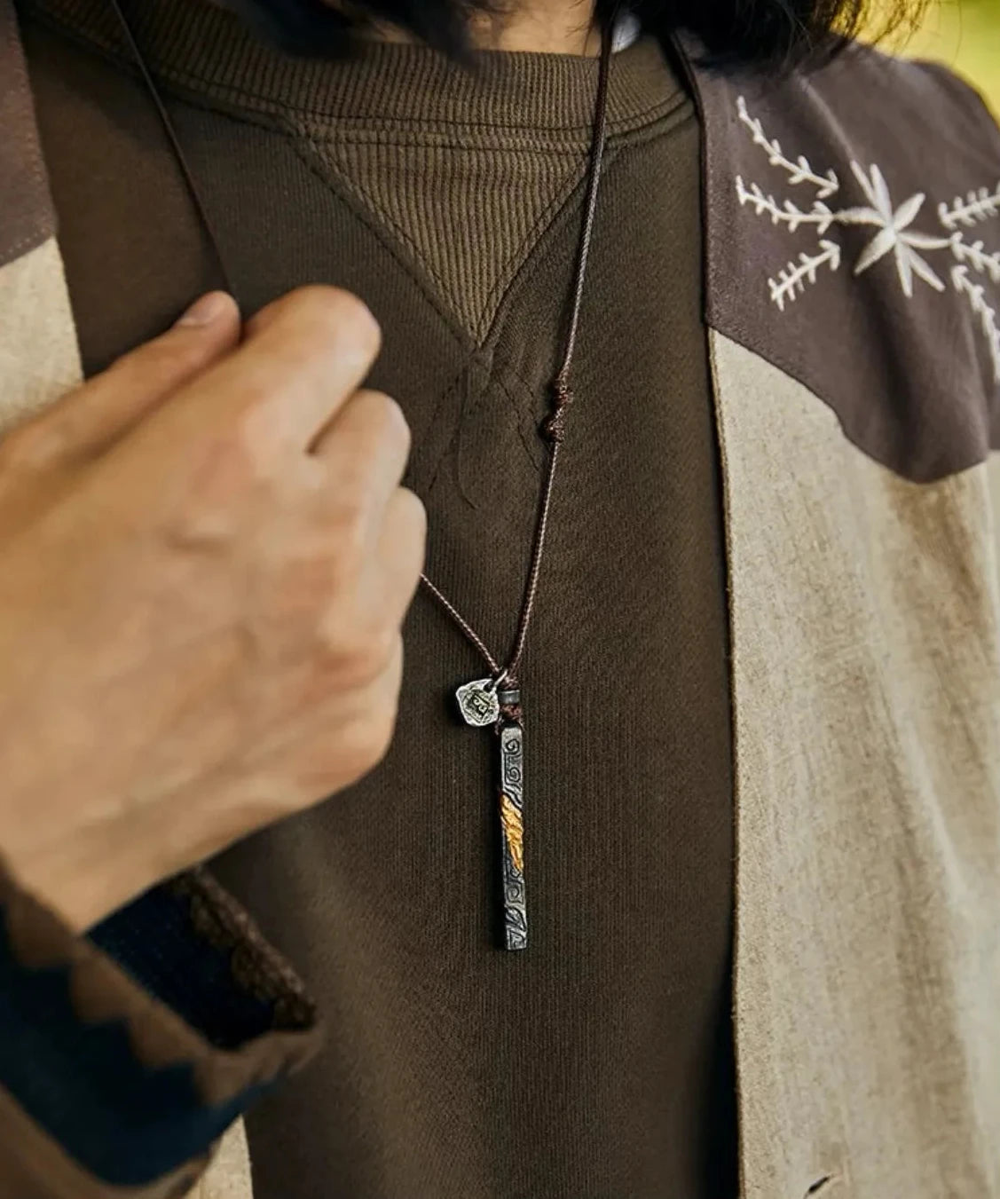 Close-up of a handcrafted oxidized silver bar pendant featuring a twisted gold accent, worn on a simple cord with earth-tone vintage clothing