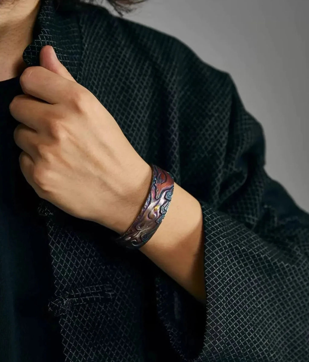 Lifestyle shot of a model holding a bag strap, wearing the colorful deer bangle paired with a dark textured jacket