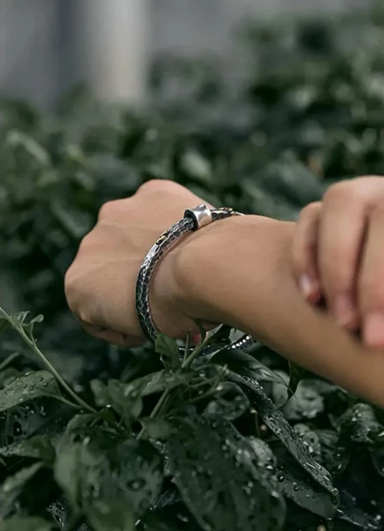 Wrist shot of the bangle against a green leafy background, emphasizing the natural and rustic aesthetic of the jewelry