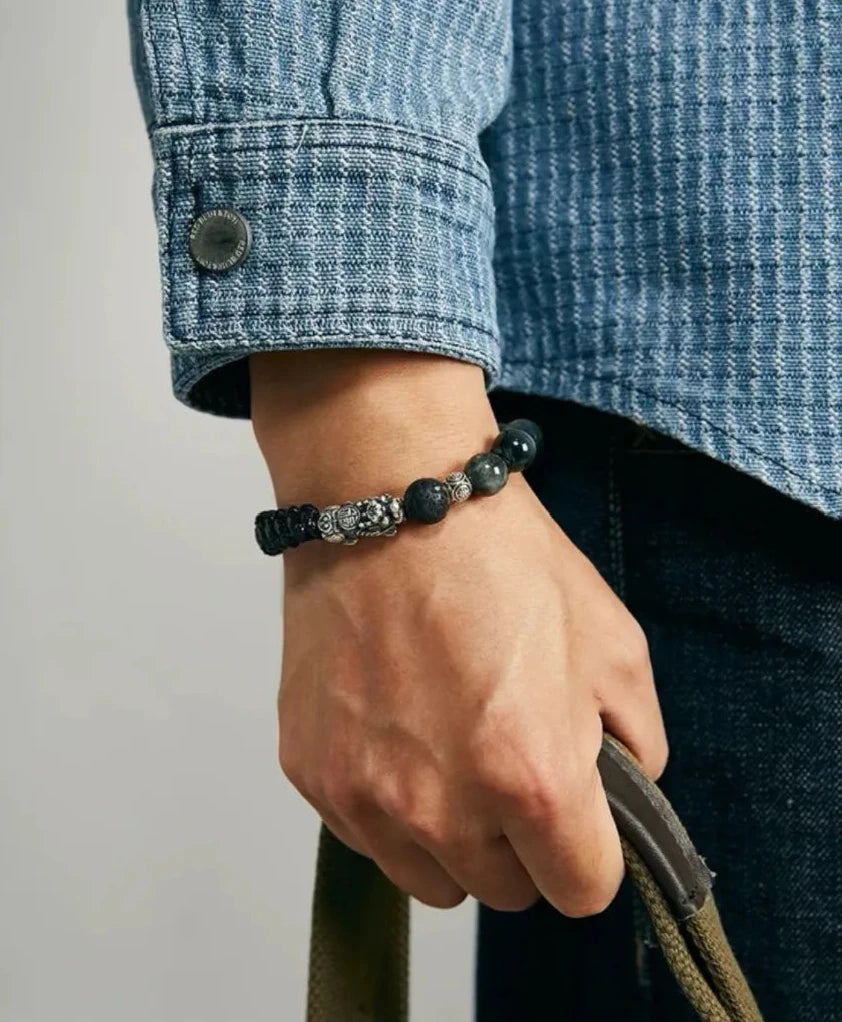 Lifestyle shot of a man in a Sashiko jacket holding a bag, wearing the blue Hawk's Eye and silver Pixiu bracele