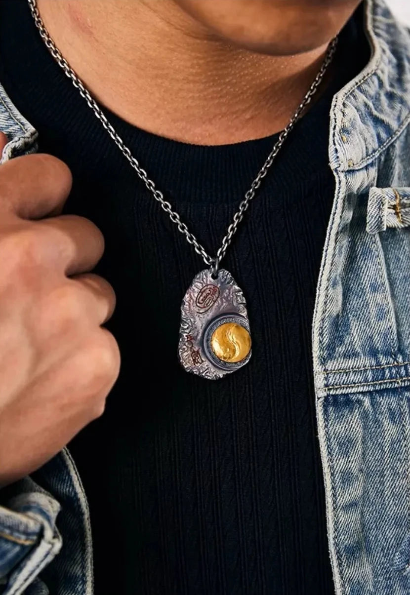 Man wearing a handcrafted rustic silver pendant with a gold Yin Yang motif, styled with a denim noragi jacket for a modern heritage look