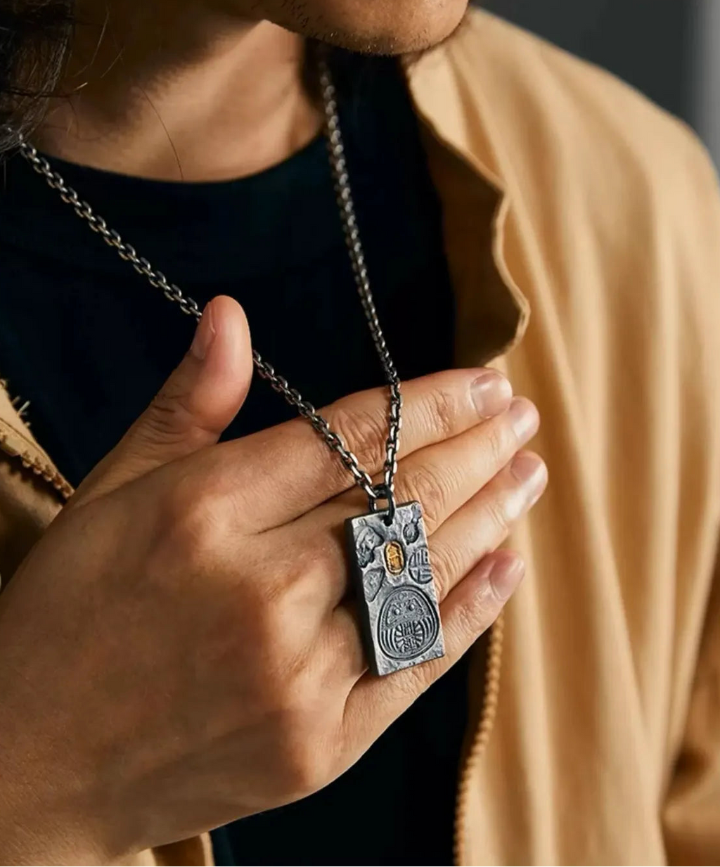 Model holding the silver Fortune Key necklace, highlighting the Daruma design and golden details against a black shirt