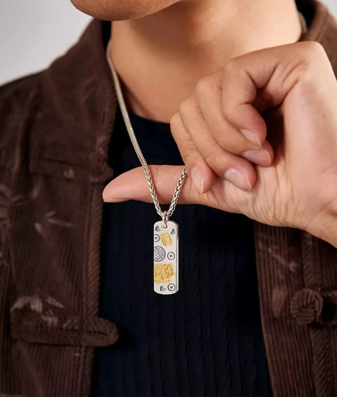Close-up of a hand holding the silver and gold lucky cat pendant, highlighting the craftsmanship