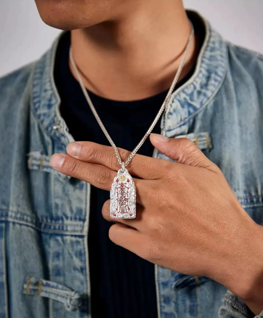 Close-up shot of a model's hand holding the Taoist cinnabar pendant to show scale and texture