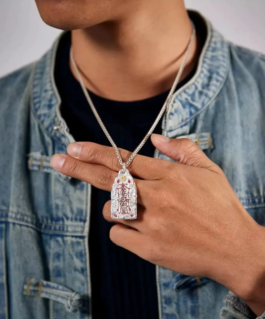Close-up shot of a model's hand holding the Taoist cinnabar pendant to show scale and texture