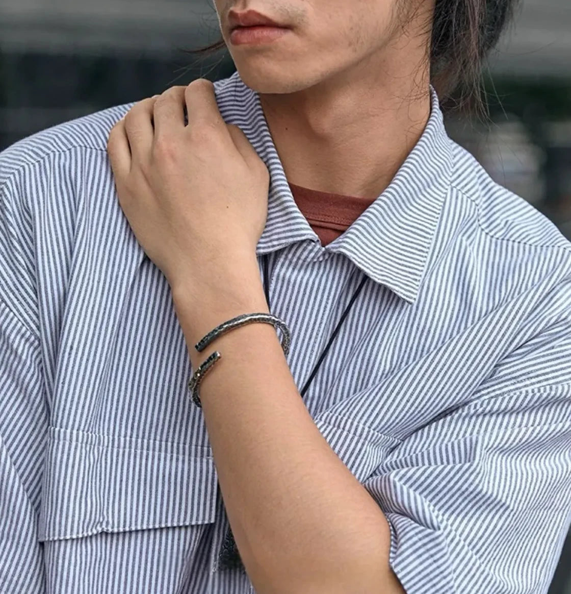 Model posing with hand on shoulder, showcasing the hammered cuff bracelet paired with a striped shirt