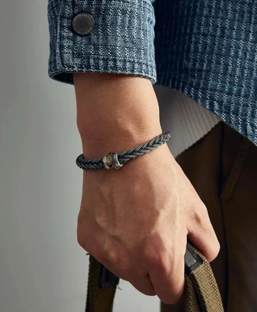 Lifestyle shot of a man in a denim jacket wearing the heavy woven silver bracelet, exuding a rugged artistic vibe