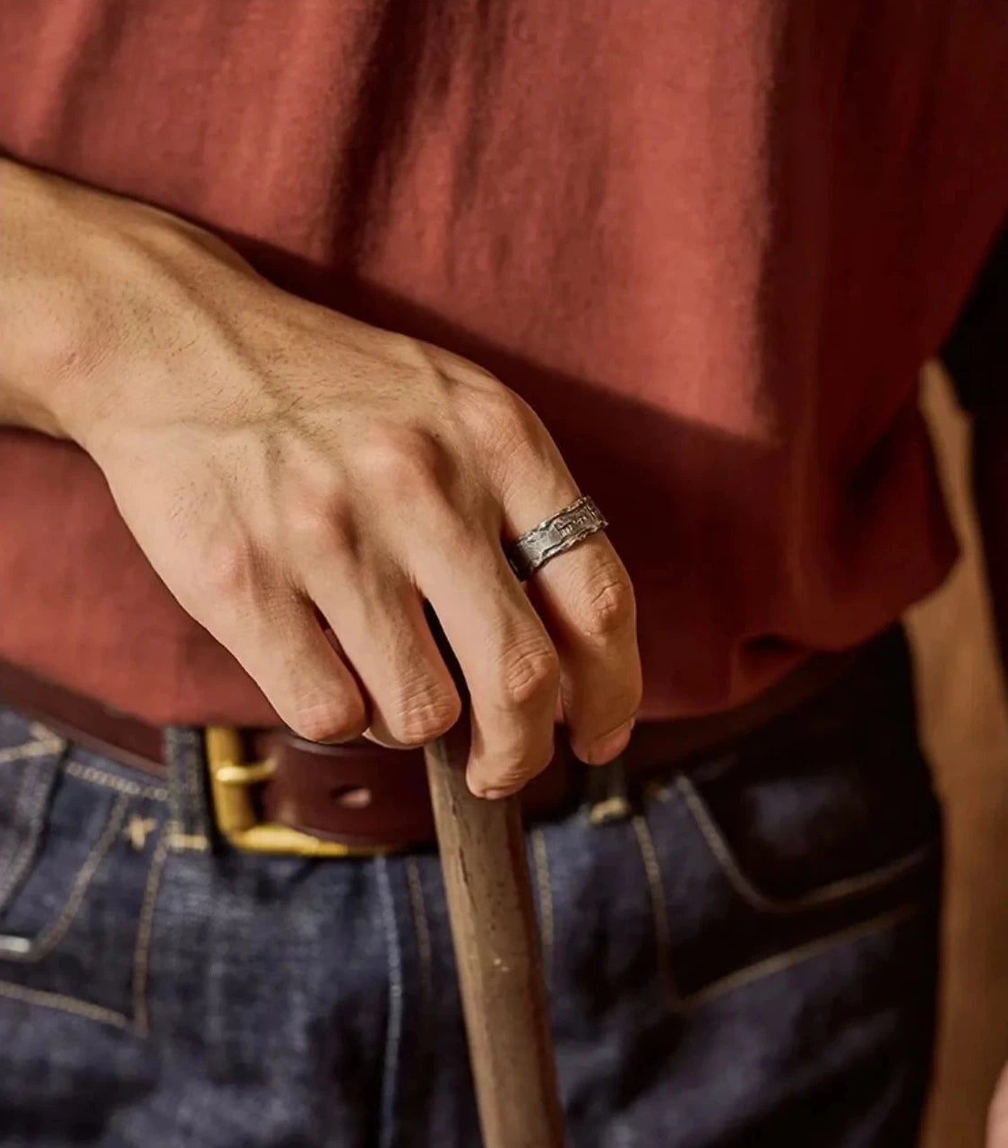Model wearing the Shift Ring with a rugged workwear outfit, holding a wooden tool handle, showcasing durability