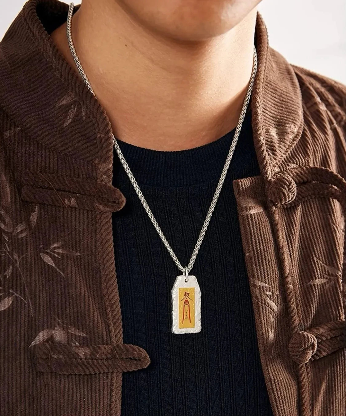 Detail shot of the silver and gold mixed metal amulet pendant hanging on a black top, showing the fit