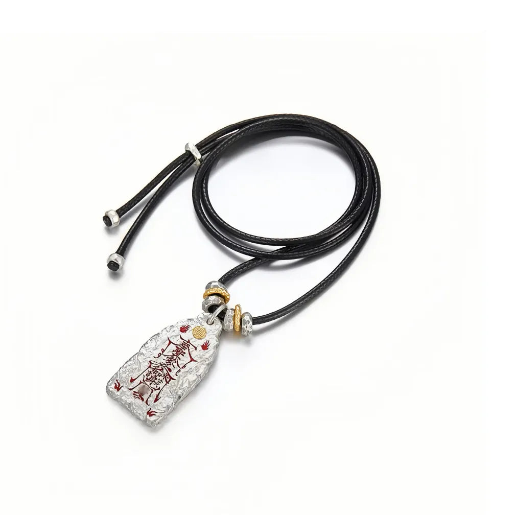 Flat lay of the Taoist protection necklace featuring a black leather cord coiled above the silver pendant