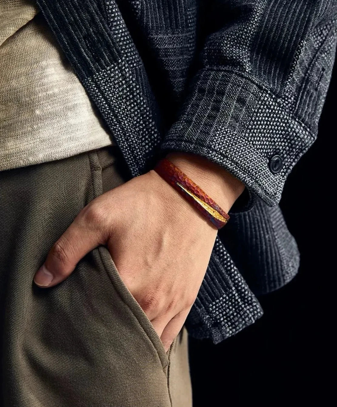 Lifestyle image of a man with his hand in his pocket, wearing the Rufous Understated Bangle which adds a pop of warm color to the dark outfit
