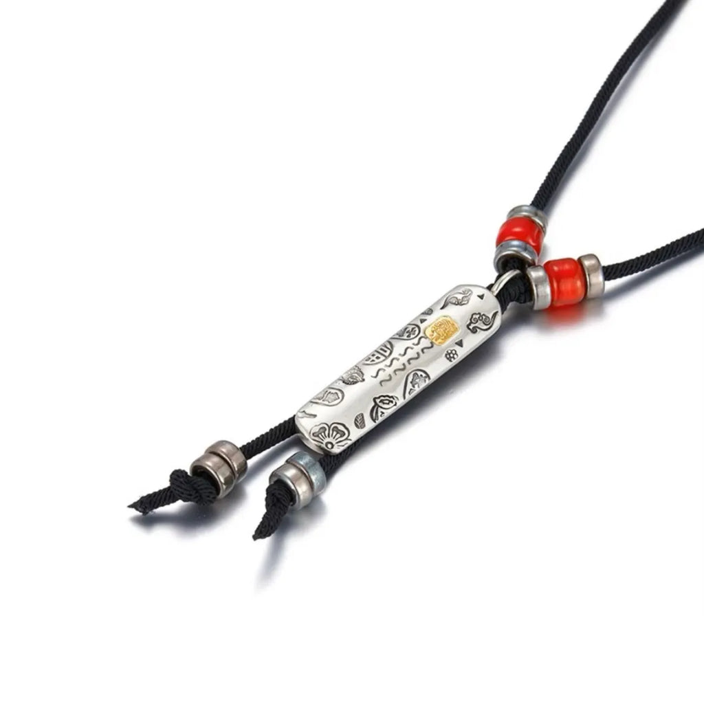 Angled shot of the silver guardian pendant, showing the detailed relief engravings and red cinnabar beads on the cord