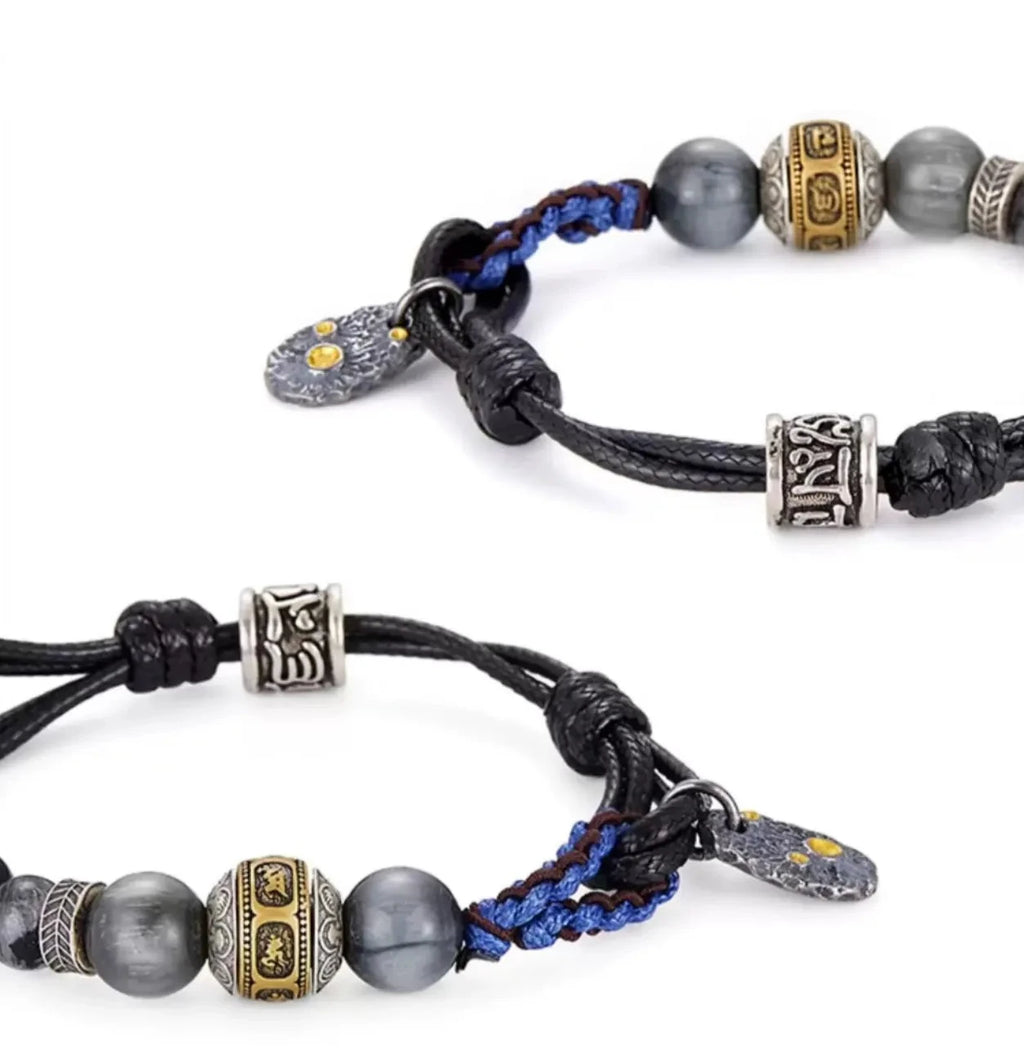 Front view of the Sunyata bracelet, featuring grey eagle eye stones and a gold-inlaid guru bead on a woven blue and black cord