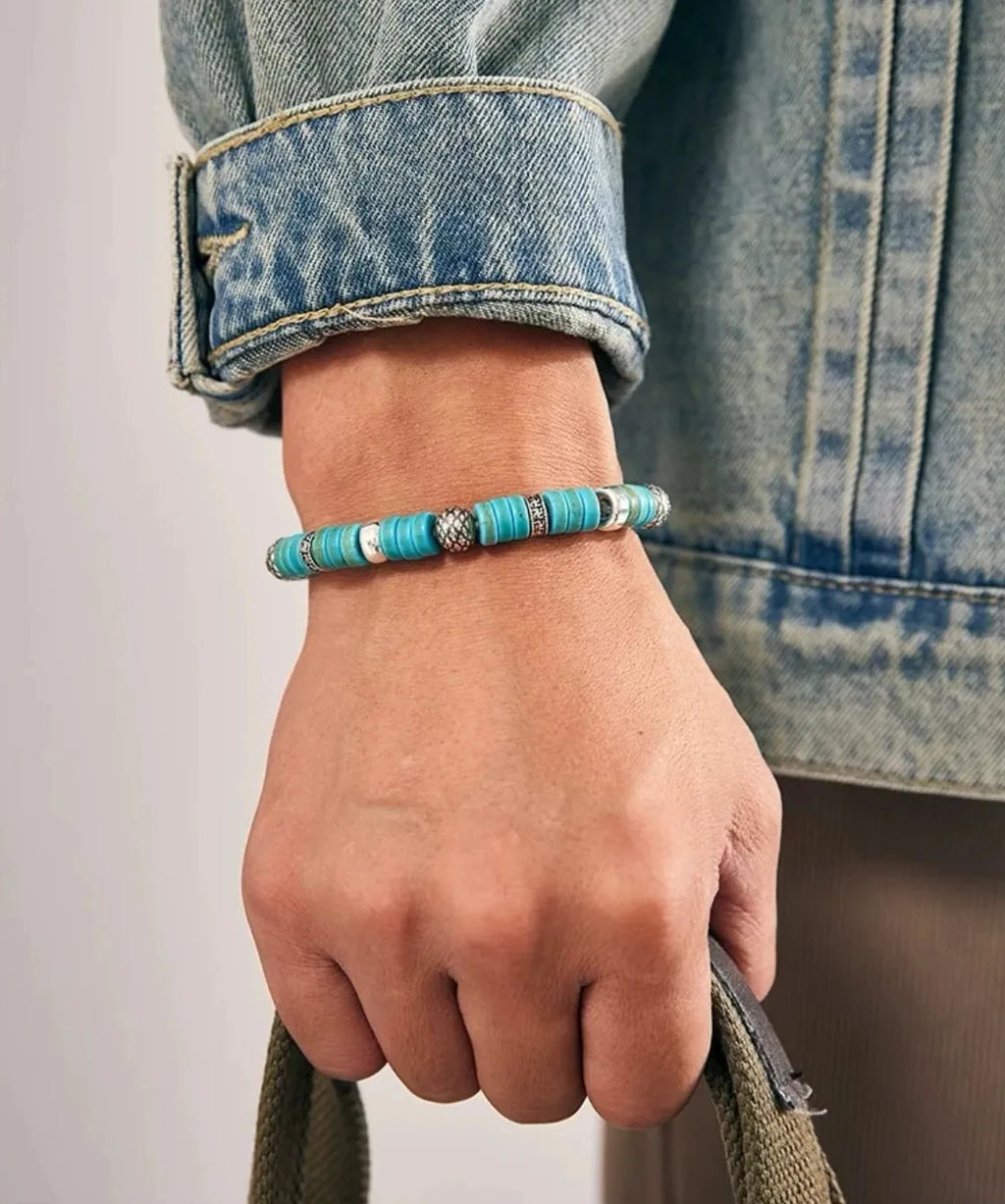 A hand holding a bag strap, demonstrating how the bright turquoise beads provide a stylish pop of color against casual denim wear