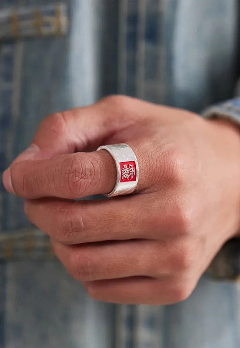 Close-up of the silver Taoist ring on a man's finger, showcasing the vibrant red square design against skin tone