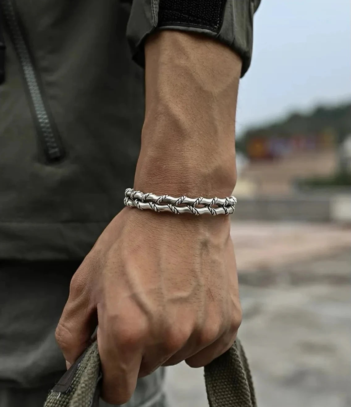 Lifestyle shot of a man's arm wearing the silver bamboo bangle, styled with a military green jacket, showcasing a rugged, masculine look